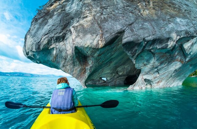 Woman sits in kayak and explores the Marble Caves and rocks on the lake of General Carrera, Chile